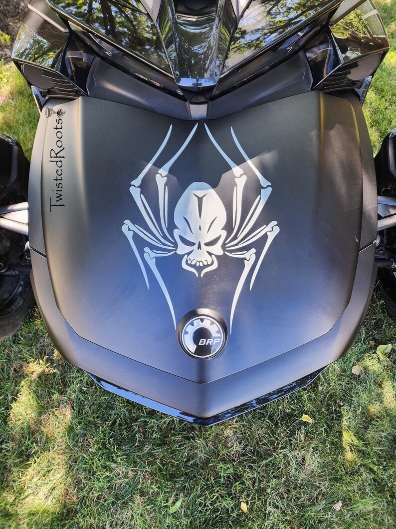 a close-up view of a motorcycle, specifically focusing on the front part of the vehicle. The motorcycle has a distinctive design, including a skull and spider motif, which is prominently displayed on the front grille.