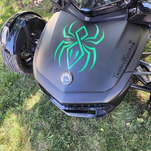 A black three-wheeled vehicle with a green spider design on the front, parked on a grassy area.
