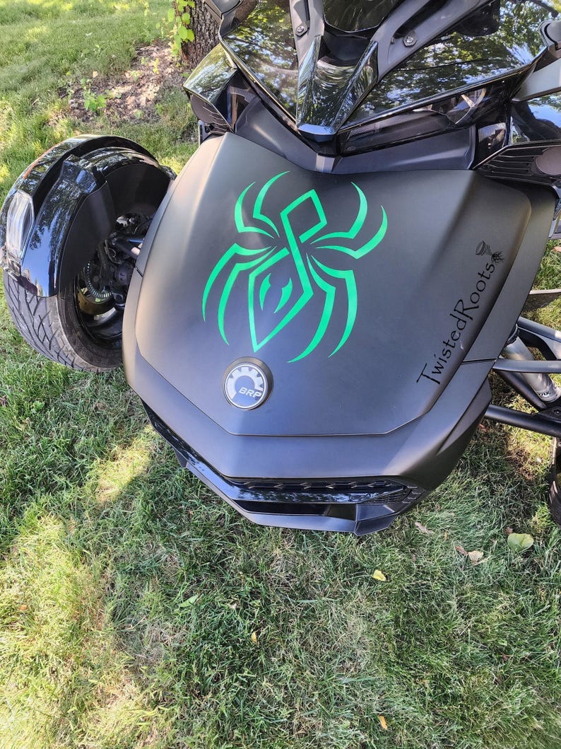 A black three-wheeled vehicle with a green spider design on the front, parked on a grassy area.