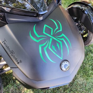 A close-up view of a motorcycle with a distinctive green and black design on the front, including a spider-like symbol.