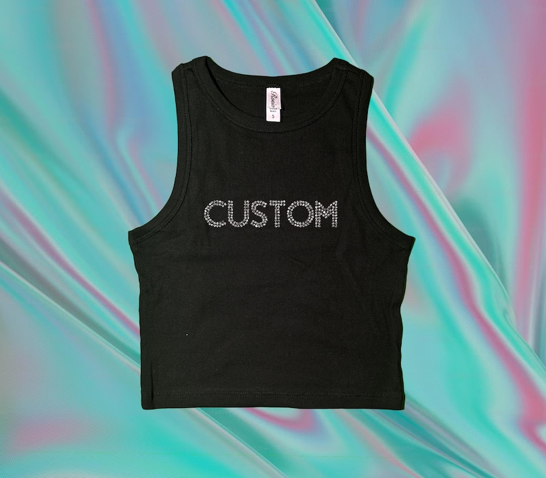 Op de afbeelding: Zwart crop top met het woord "CUSTOM" in strass steentjes op de voorkant. De top is mouwloos met een ronde hals en een klein labeltje bij de halslijn.