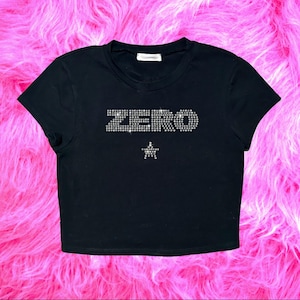May include: Black crop top with the word "ZERO" spelled out in rhinestones. A rhinestone star is below the word. The top has short sleeves and a crew neck.