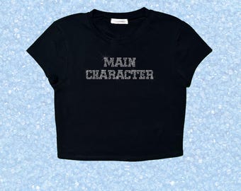 Top corto con pedrería "PERSONAJE PRINCIPAL", camiseta estilo Y2K con eslogan brillante, camiseta personalizada con pedrería, top llamativo con purpurina, atuendo para fiestas y festivales.