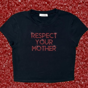 Pode incluir: Top preto curto com a frase "RESPECT YOUR MOTHER" em strass vermelhos. A camisa tem gola redonda e mangas curtas. O fundo &eacute; uma superf&iacute;cie vermelha texturizada.