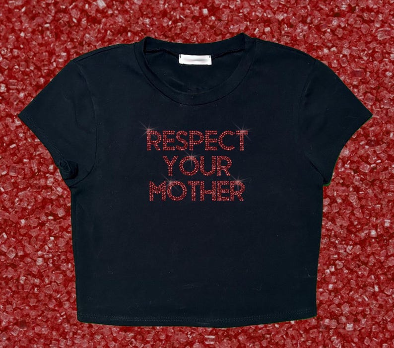 Pode incluir: Top preto curto com a frase "RESPECT YOUR MOTHER" em strass vermelhos. A camisa tem gola redonda e mangas curtas. O fundo &eacute; uma superf&iacute;cie vermelha texturizada.