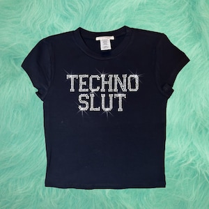May include: A black short-sleeved t-shirt with the words "TECHNO SLUT" in rhinestones.