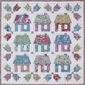 May include: A white quilt with a patchwork design featuring a variety of floral fabrics. The quilt is made up of nine squares, each containing a small house with a different floral pattern. The houses are surrounded by a border of smaller squares with floral patterns.