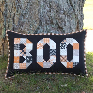 May include: A black pillow with a white and orange patchwork design spelling out "BOO".