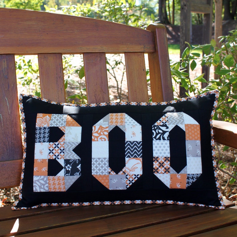 May include: A black and white pillow with the word "BOO" spelled out in orange and gray patchwork fabric.