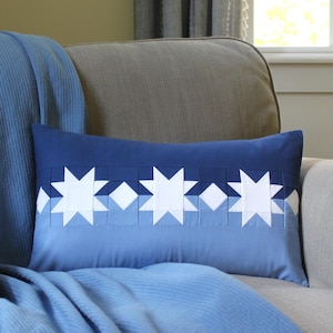 Könnte beinhalten: Ein blaues und weißes Kissen mit einem Muster aus weißen Sternen auf blauem Hintergrund. Das Kissen liegt auf einem grauen Sofa mit einer blauen Decke.