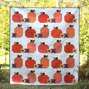 May include: A white quilt with a patchwork design featuring orange, red, and brown pumpkins with small purple and yellow flowers. The quilt is hanging on a clothesline outdoors.