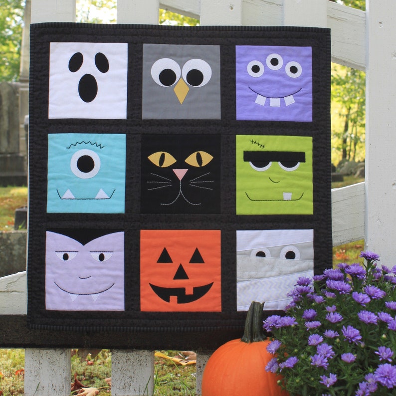 May include: A Halloween-themed quilt with nine square panels, each featuring a different monster face. The faces include a ghost, owl, three-eyed monster, one-eyed monster, cat, Frankenstein, vampire, jack-o'-lantern, and mummy. The quilt is black with a white picket fence in the background.