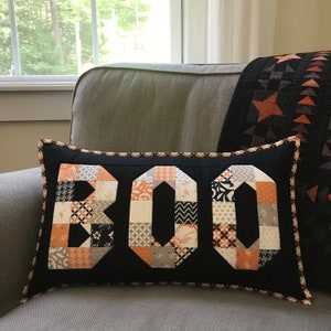 May include: A black and white pillow with the word "BOO" spelled out in orange and white patchwork fabric.