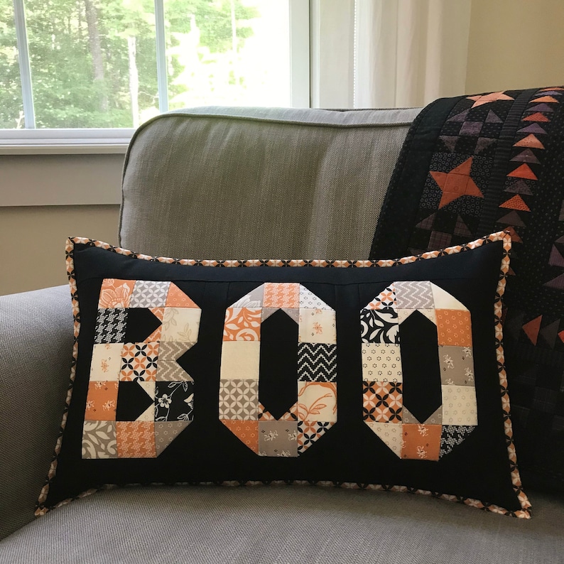 May include: A black and white pillow with the word "BOO" spelled out in orange and white patchwork fabric.