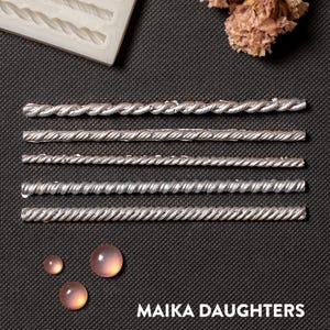 May include: Six silver, rope-like, decorative metal strips on a black background. The strips are arranged vertically, with the largest at the top and the smallest at the bottom. The image also includes three pink, round, decorative stones.