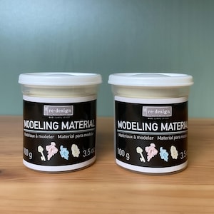 May include: Two containers of modeling material with white lids and black labels. The labels read "MODELING MATERIAL" and include the text "Matériaux à modeler Material para modelar". Each container holds 100 g / 3.5 oz of material.