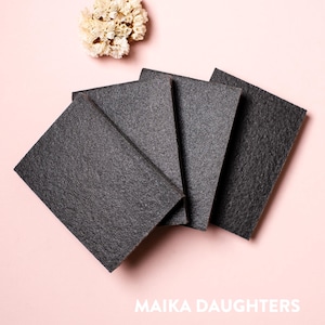 May include: Four black rectangular pieces of charcoal soap on a pink background. The soap is rough and textured. The text "MAIKA DAUGHTERS" is printed on the bottom of the image.
