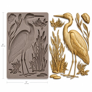 May include: A silicone mold and a finished casting of a heron, reeds, and floral elements. The mold is 8 inches (20.3 cm) tall and 5 inches (12.7 cm) wide. The finished heron is gold-colored and stands among detailed plant life.