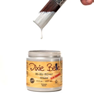 May include: A silver jar of Dixie Belle Hi-Ho Silver Glaze paint with a brush dipped in the paint and dripping. The jar is labeled with the product name, size, and "New Formula".