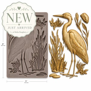 May include: A gray silicone mold with a heron design, measuring 8 inches (20.3 cm) high and 5 inches (12.7 cm) wide, alongside a gold heron and plant embellishments. The mold includes the text "NEW JUST ARRIVED at Maika Daughters".