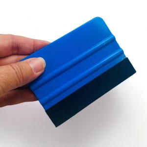 May include: A blue plastic squeegee with a black felt edge. The squeegee has two raised lines on the surface.