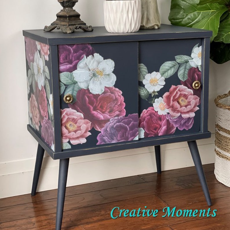 A vintage side table with 2 sliding doors refurbished by Creative Moments is painted a soft, dark blue and features the Floral Romance transfer.