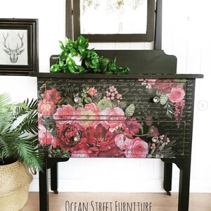 A vintage dresser painted black with roses across the front in different shades of pink. On the bottom, in black lettering, it reads Ocean Street Furniture.