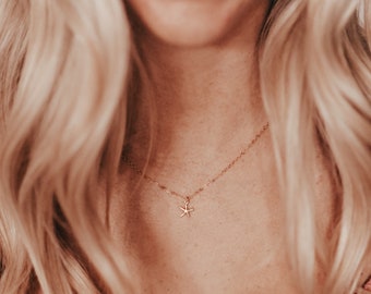 May include: A delicate gold-colored necklace featuring a small starfish pendant. The necklace is worn around the neck, with the pendant resting on the chest. The chain is thin and the starfish has a detailed design.