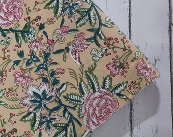 May include: A beige fabric with a floral print featuring pink, green, and white flowers. The fabric has a traditional Indian design.