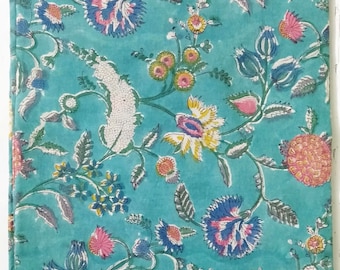 May include: A turquoise fabric with a floral pattern. The design features blue, pink, yellow, and white flowers with green leaves and stems. The fabric has a textured appearance, with the flowers and leaves arranged in a flowing, organic pattern.