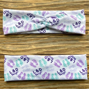 May include: Two white headbands with a purple and teal footprint pattern and the text "L&D nurse" repeated throughout.