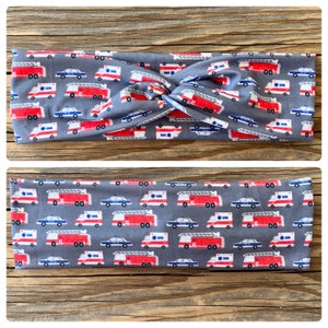 May include: Two gray headbands with a repeating pattern of red fire trucks, white ambulances, and blue police cars. The headbands are made of a soft fabric and are designed to be worn around the head.
