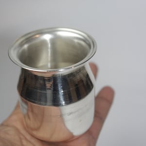 May include: A silver, shiny, traditional Indian water pot with a rounded body and a flared rim.