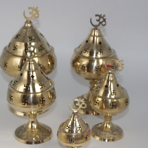 May include: Set of four gold-colored brass oil lamps with intricate swastika designs and Om symbols. The lamps are of varying sizes and have a conical shape with a round base.