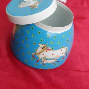 May include: A blue decorative jar with a white interior and lid. The jar and lid feature a repeating pattern of small yellow dots and a white horse illustration with red spots. The lid has a clear, round knob.