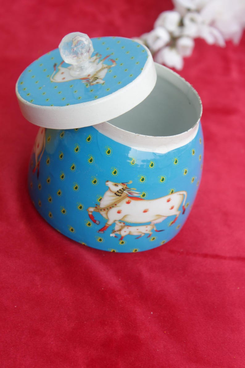 May include: A blue decorative jar with a white interior and lid. The jar and lid feature a repeating pattern of small yellow dots and a white horse illustration with red spots. The lid has a clear, round knob.