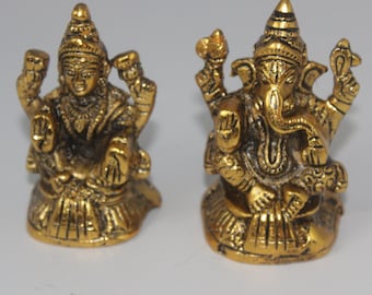 May include: Two small gold-colored metal statues of Hindu deities. The statue on the left is of Lakshmi, the goddess of wealth and prosperity. The statue on the right is of Ganesha, the elephant-headed god of beginnings and remover of obstacles.