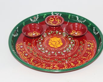 May include: A red and green metal plate with a decorative design featuring a yellow Ganesha figure. The plate has four small red bowls around the center.