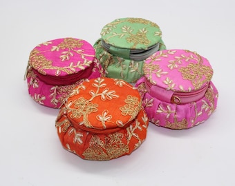 May include: Four round, fabric-covered boxes with gold embroidery and zipper closures. The boxes are in shades of pink, green, and orange.