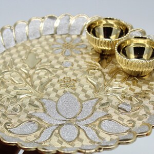 May include: A gold and silver decorative tray with a floral design and two small bowls. The tray has a scalloped edge and a textured surface.