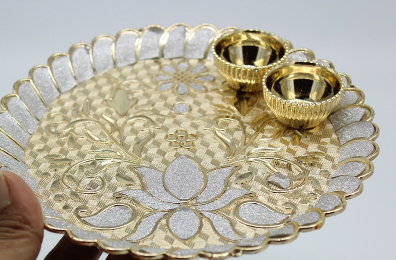 May include: A gold and silver decorative tray with a floral design and two small bowls. The tray has a scalloped edge and a textured surface.