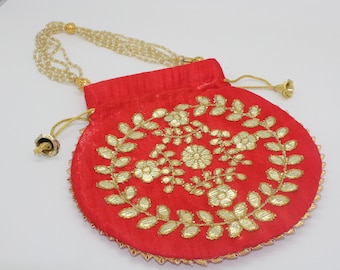 May include: A red drawstring bag with gold embroidery of floral designs and leaves. The bag has a beaded strap.