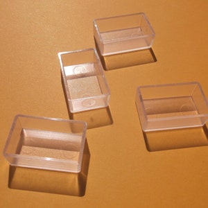 May include: Four clear plastic rectangular boxes with rounded corners. The boxes are empty and have a slight sheen.