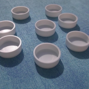 May include: Eight white round plastic containers with a smooth surface. The containers are arranged in a circle on a blue textured surface.