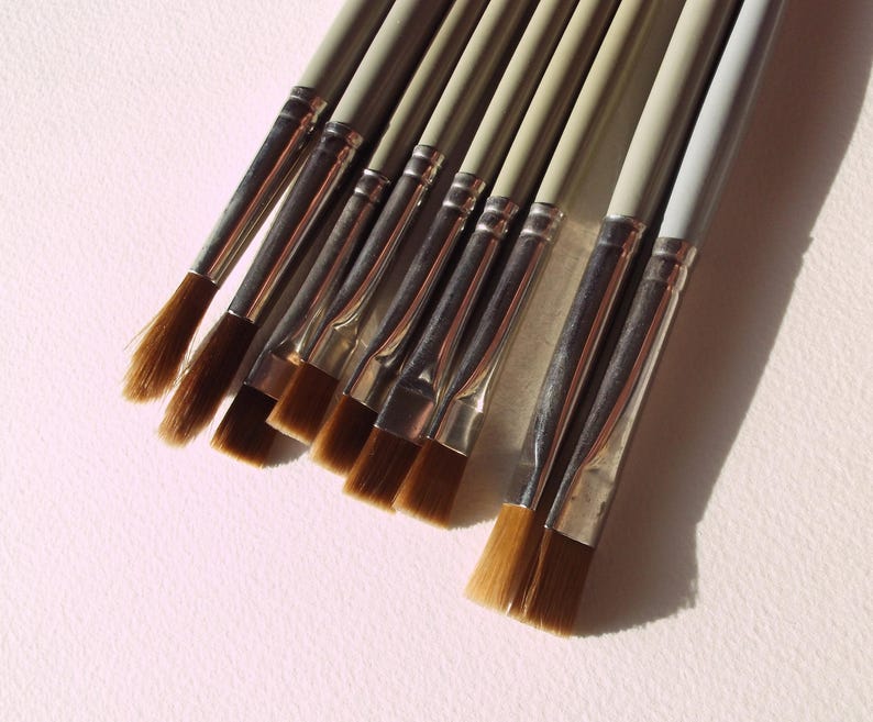 May include: A set of nine paint brushes with brown bristles and silver metal ferrules. The brushes are arranged in a row, with the largest brush on the left and the smallest brush on the right.