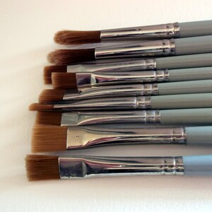 May include: A set of eight paint brushes with silver metal ferrules and light blue wooden handles. The brushes have different sizes and shapes of bristles.