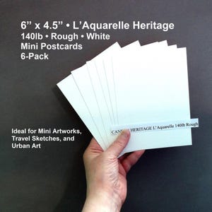 May include: A stack of six white mini postcards, each measuring 6" x 4.5", held by a hand. The postcards are labeled "L'Aquarelle Heritage 140lb Rough White" and are designed for mini artworks, travel sketches, and urban art.
