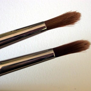 May include: Two paint brushes with silver handles and brown bristles. The brushes are different sizes.