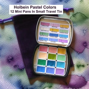 May include: An open, small, silver travel tin containing 12 mini Holbein pastel watercolor pans. The tin is next to a purple velvet drawstring bag. The text "Holbein Pastel Colors 12 Mini Pans In Small Travel Tin" is at the top of the image.