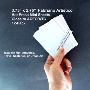 May include: A stack of white Fabriano Artistico Hot Press Mini Sheets, measuring 3.75" x 2.75", held in a hand. The pack contains 12 sheets, suitable for mini artworks, travel sketches, or urban art. The label reads "Fabriano Artistico - Watercolor Paper".